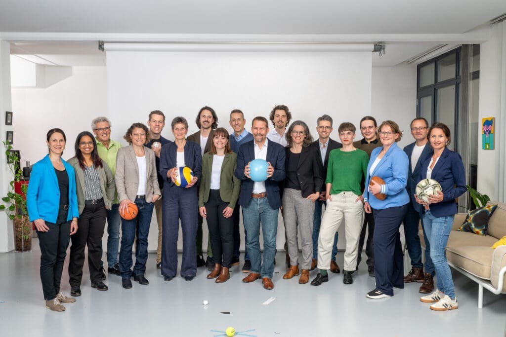 Gruppenbild mit 18 der Kandidierenden. In der Mitte Gemeinderat Thomas Marti. Einige tragen Bälle (von Basketball bis Fussball).